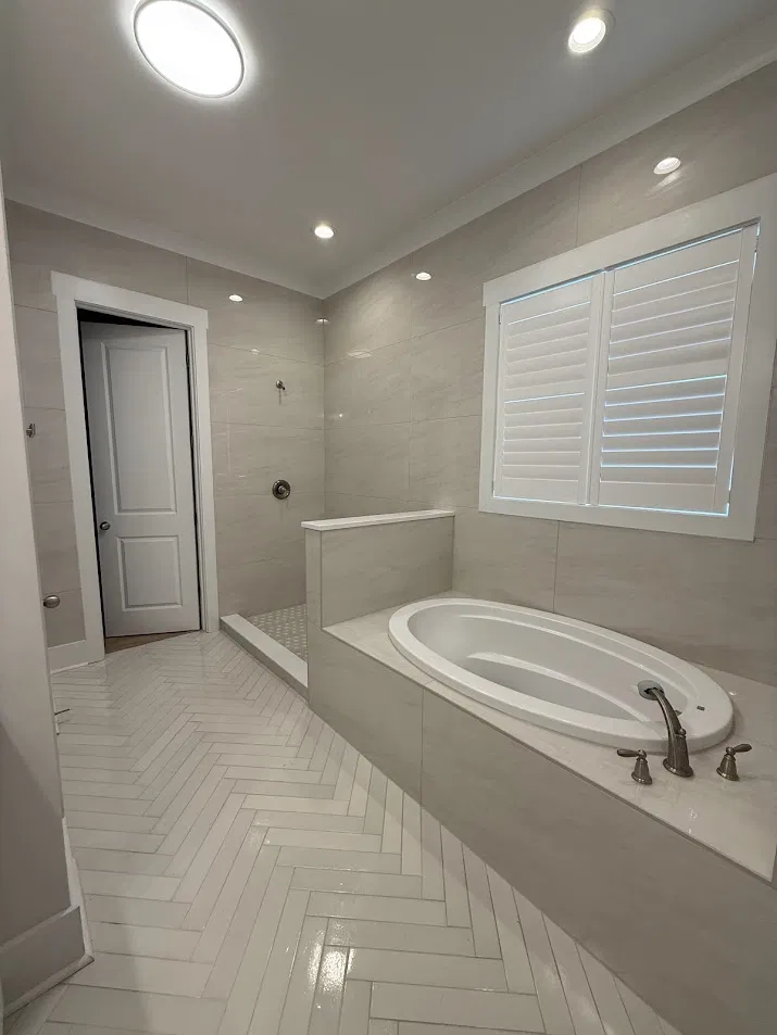 Bathroom with herringbone floor tile, soaking tub, and large format wall tile by CNB Renovations